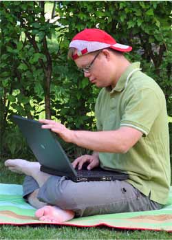 Dominic mit Sonnenhut im Garten, am Laptop sitzend